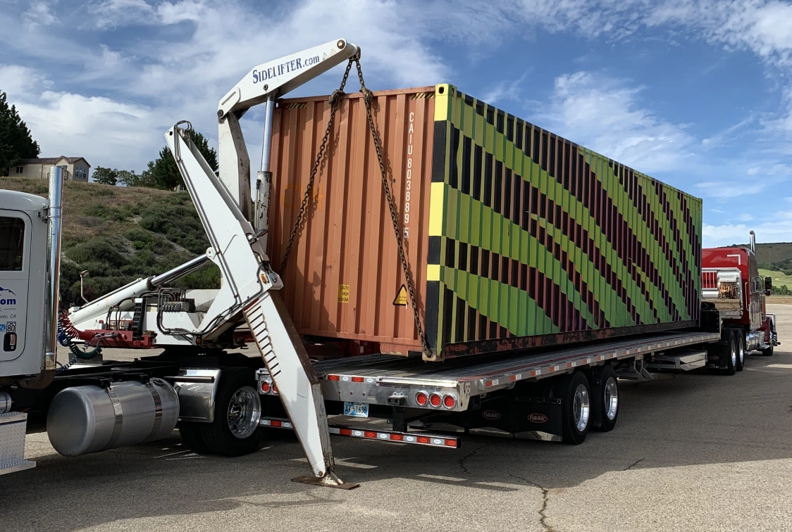 Semi truck with a crane on the back of it, transporting a container