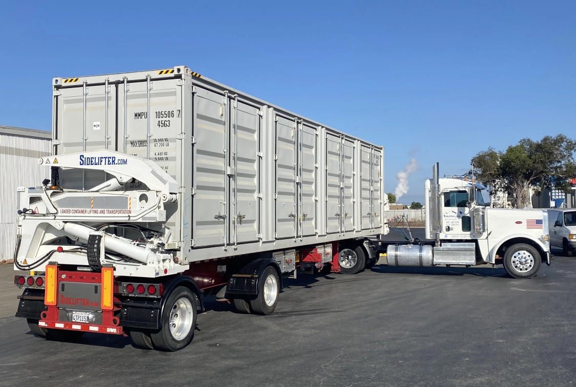 White truck parked in a parking lot next to a building, with a container on the back of it