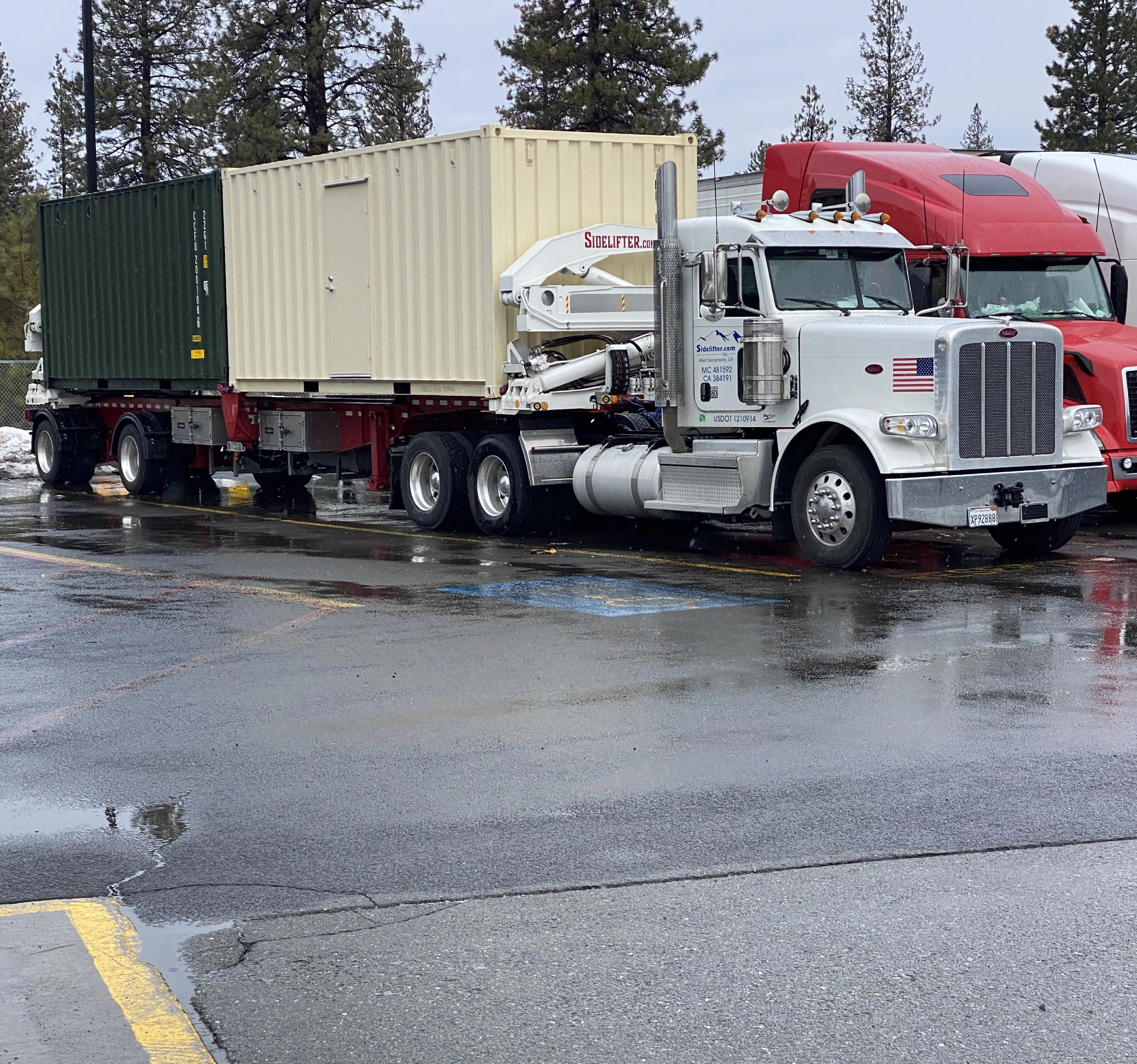 Semi truck with a trailer on the back of it driving down a road surrounded by trees, poles