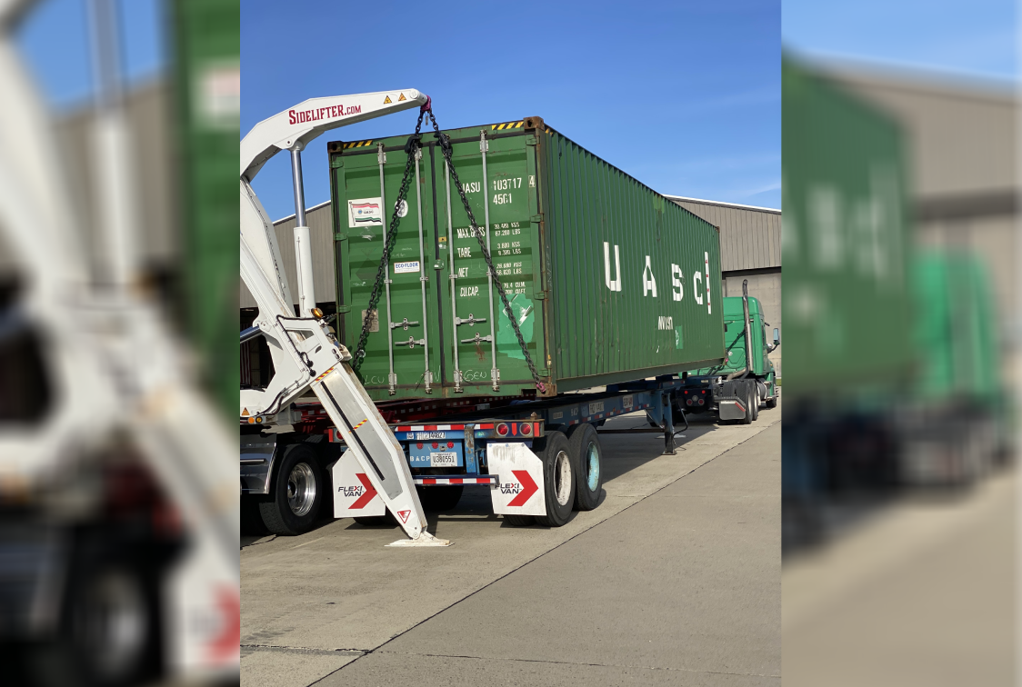 Truck with a green container on the back of it, parked in front of a building